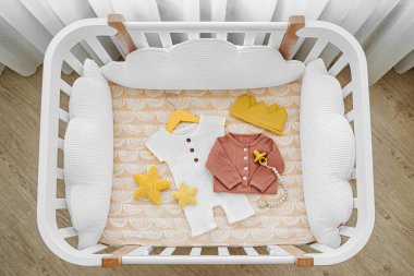 Bebek kıyafetlerinin ve beşikteki aksesuarların en üst görüntüsü. Bebek odasında beyaz yastıklı yeni doğan için ahşap beşik..  