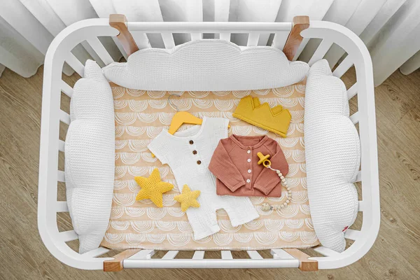 Bebek kıyafetlerinin ve beşikteki aksesuarların en üst görüntüsü. Bebek odasında beyaz yastıklı yeni doğan için ahşap beşik..  
