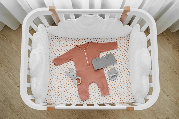 White wooden baby crib with pillows shaped clouds  in baby\'s room. Newborn clothes and accessories in cot. Top view of child\'s bed