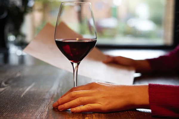 Woman holding a glass of red wine in restaurant or cafe on wooden table in front of window, romantic date, lunch relaxation