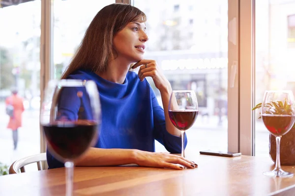 Beautiful woman drinking red wine with friends in cafe, portrait with wine glass near window. Vocation holidays bar concept