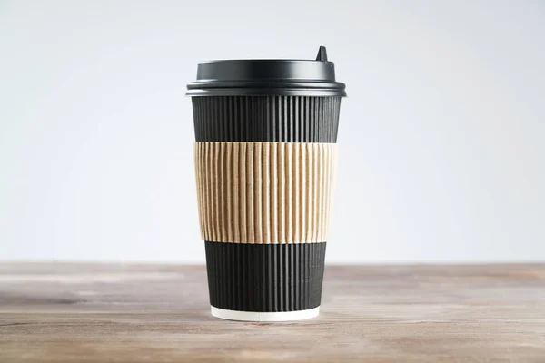 Paper disposable coffee black cup for take away or to go, at wooden table, space for design layout.