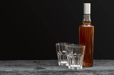 Siyah arka planda iki boş bardak olan bir şişe viski. Metin için boşluk.