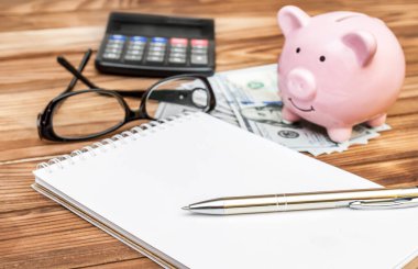 Masanın üzerinde kumbara, para ve hesap makinesi olan boş bir not defteri. 