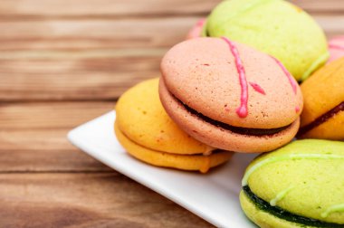 Ahşap masada renkli badem kurabiyesi tabağı. Kapat..