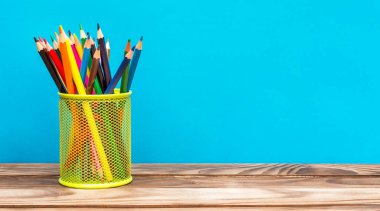 Mavi arka plandaki ahşap masada renkli kalemleri olan tutucu. Metin için boşluk.