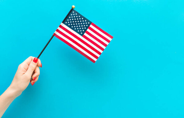 Woman's hand holding small american flag on blue background. Space for text.