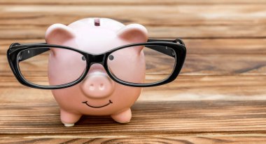 Ahşap arka planda gözlüklü domuz kumbarası.