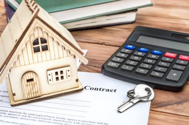 Ahşap masada anahtar, hesap makinesi ve not defterleriyle iş sözleşmesi üzerine ev modeli.