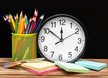 Tutacağında renkli kalemler olan saat ve tabloyu karatahtaya yapıştırıyor. Okul zamanı..