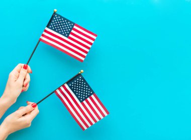Mavi arka planda küçük Amerikan bayrakları tutan kadınların elleri. Metin için boşluk.