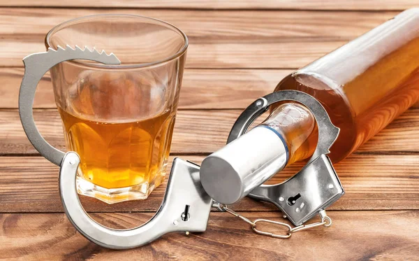ボトルとガラス アルコール飲料と木製のテーブルの上に手錠 アルコール依存症 — ストック写真
