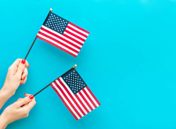 Woman's hands holding small american flags on blue background. Space for text.
