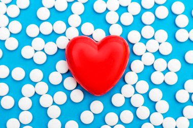 Red heart with white pills on blue. Medical background. Top view.  clipart