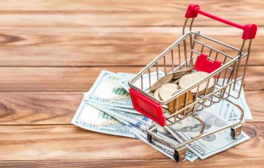 Tahta masa üzerinde para ve dolarlarla dolu alışveriş arabası..