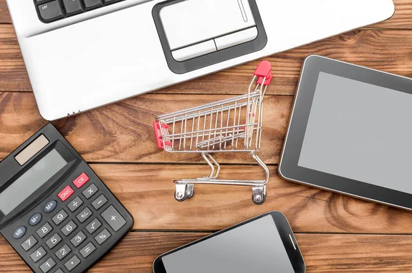 Shopping cart and electronic devices on the wooden background. Top view. Online shopping concept.