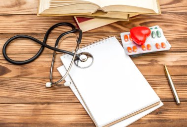 Steteskoplu boş not defteri, haplar, kırmızı kalp ve masanın üzerinde bir yığın kitap. Doktorun işyeri..