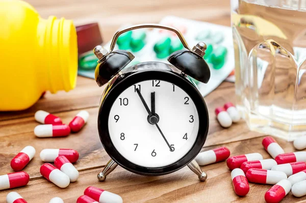 Clock with pills and glass of water on the table. Close up.