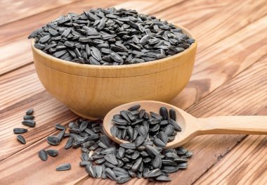 Tahta sehpa üzerinde ayçiçeği tohumları olan tahta kase ve kaşık. Kapat..