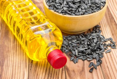 Ahşap zemin üzerinde bir kase ayçiçeği çekirdeği olan plastik bir yağ şişesi.. 