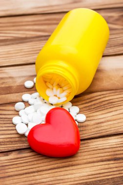 Plastik şişeden saçılan haplar ve ahşap arka planda kırmızı kalp..