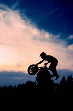 Gün batımında bir motosikletçinin silueti. Moto sürücüsü motosikletini kullanıyor..