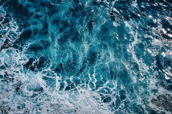Okyanustaki su sıçrayan dalgaların hava görüntüsü. Mavi, temiz, dalgalı deniz suyu. Köpüklü sallanan dalgalar.