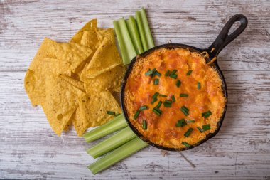 Cips ve kereviz ile baharatlı bufalo tavuk peynir dip ile bir tavada, düz yatıyordu