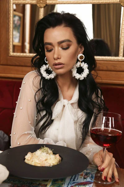 sensual woman with dark hair in elegant clothes and earrings sit