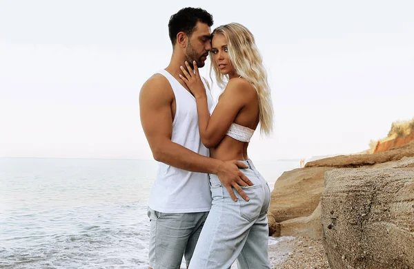 Hermosa pareja encantadora con pantalones vaqueros, posando en la playa de verano — Foto de Stock