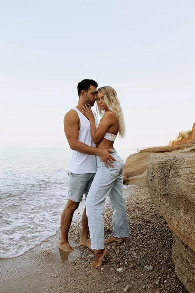 Hermosa pareja encantadora con pantalones vaqueros, posando en la playa de verano — Foto de Stock