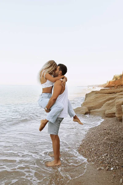 Hermosa pareja encantadora con pantalones vaqueros, posando en la playa de verano — Foto de Stock