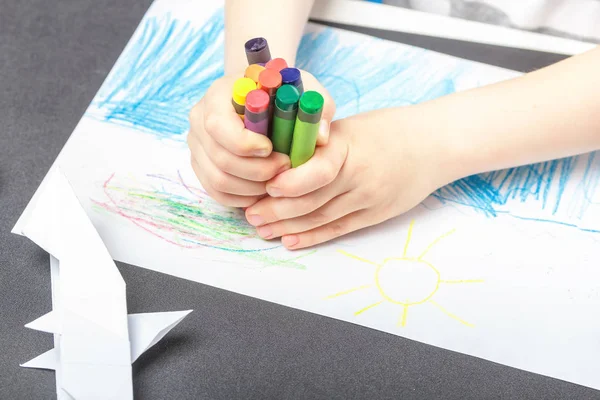 Drawing on a white sheet of paper with colored wax pencils. The concept of children\'s creativity and hobbies. The child draws a set of colored pencils abstract lines and patterns. Baby hands closeup