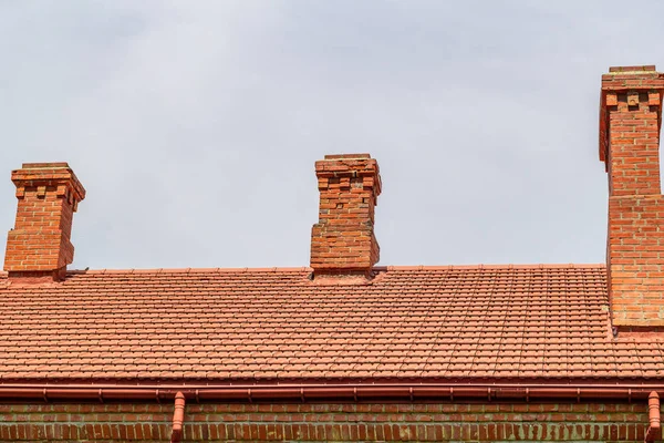 曇り空の背景にレンガの煙突と新しいタイルで覆われた屋根 — ストック写真