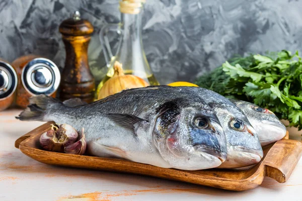 Üç ham kılıçbalığı bir ahşap tepsi otlar, limon, soğan, sarımsak, baharatlar ve zeytinyağı dokulu gri bir arka plan üzerinde balık pişirmek hazır