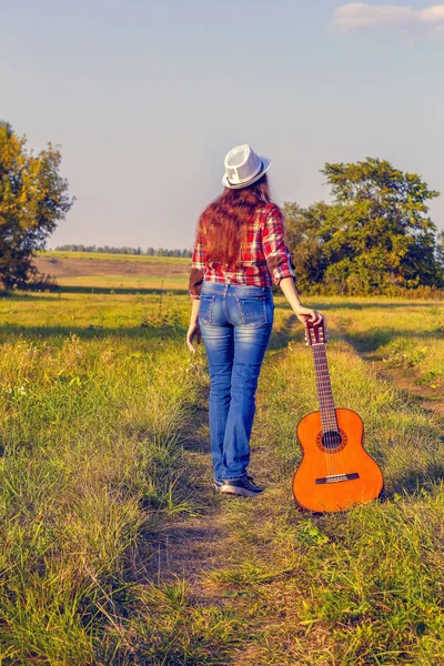 Vacker, glad, rödhårig flicka i ett fält på en solnedgång bakgrund med en gitarr på sommaren. Begreppet enhet för den kreativa personen med naturen — Stockfoto