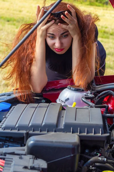 Genç bir kadın araba ile yükseltilmiş bir kukuleta ile standları ve şaşkın, otomobilin motora arıyorum. Yolda araba arızası
