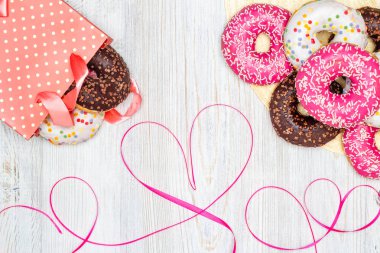 Çörek, hediye çanta içinde donut ve ahşap masa üzerinde kırmızı kurdele kalp ile. Düz yatıyordu. Sevgililer günü kutlama kavramı