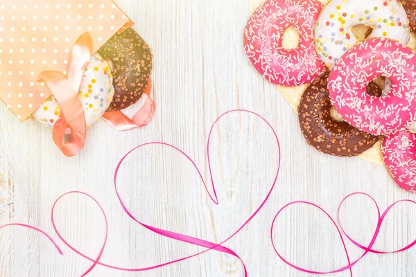 Donuts, gift bag with donuts inside and a red ribbon heart on a wooden table. Flat lay. Valentine\'s Day celebration concept.