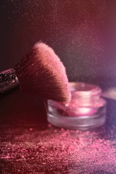 Rosa skuggor, glitter på den kosmetiska borsten och en burk med lock på en mörk bakgrund — Stockfoto