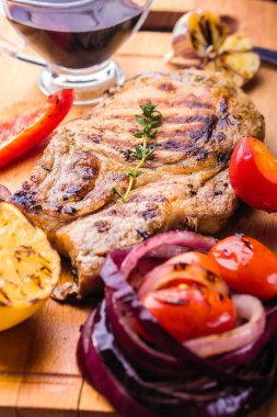 Bir ahşap tahta üzerinde sulu domuz biftek fışkın taze kekik, limon ve ızgara sebzeler ve sos ile servis