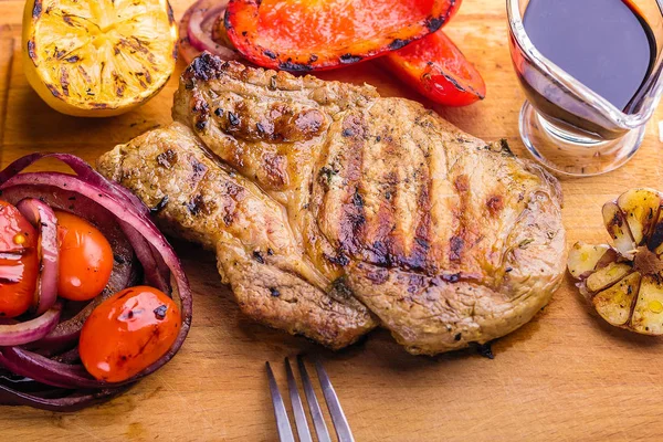 Carne de cerdo jugosa con una ramita de tomillo fresco, limón y verduras a la parrilla y salsa servida en una tabla de madera — Foto de Stock