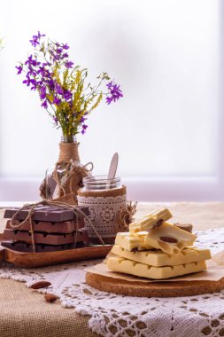 Karanlık, sütlü ve beyaz çikolata, yemekler ve pencere karşı yaban çiçekleri buket ile hala hayat. Boşluk Kopyala