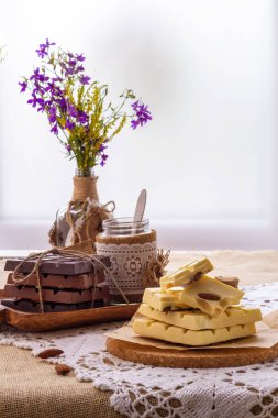 Karanlık, sütlü ve beyaz çikolata, yemekler ve pencere karşı yaban çiçekleri buket ile hala hayat. Boşluk Kopyala