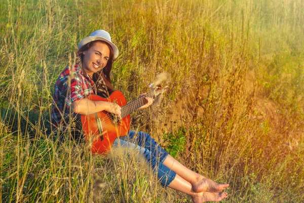 Krásná, šťastná žena v létě v paprscích západu slunce s kytarou. Koncept tvůrčí svobody, zábavy a letních prázdnin — Stock fotografie