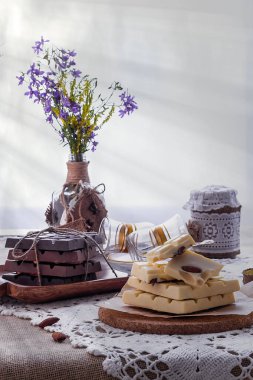 Karanlık, sütlü ve beyaz çikolata, yemekler ve pencere karşı yaban çiçekleri buket ile hala hayat. Boşluk Kopyala