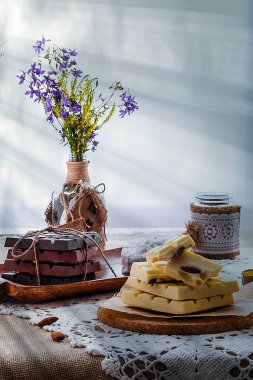 Karanlık, sütlü ve beyaz çikolata, yemekler ve pencere karşı yaban çiçekleri buket ile hala hayat. Boşluk Kopyala