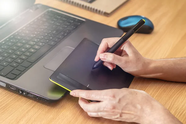 Illustrator using a graphics tablet. Womans retouchers hands using laptop and drawing tablet