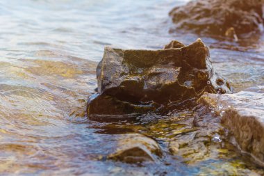 Nehre yakın taş. Dalgalar kıyı şeridinde akıtar. Yaz gün batımı. Güneş ışınları suya yansır.