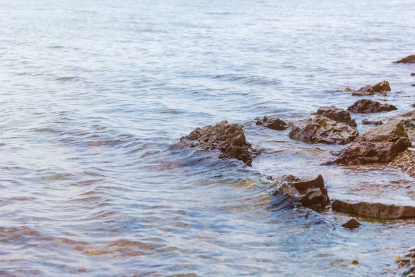 Piedra cerca del río. Las olas corren en la costa. Puesta de sol de verano. Los rayos del sol se reflejan en el agua —  Fotos de Stock